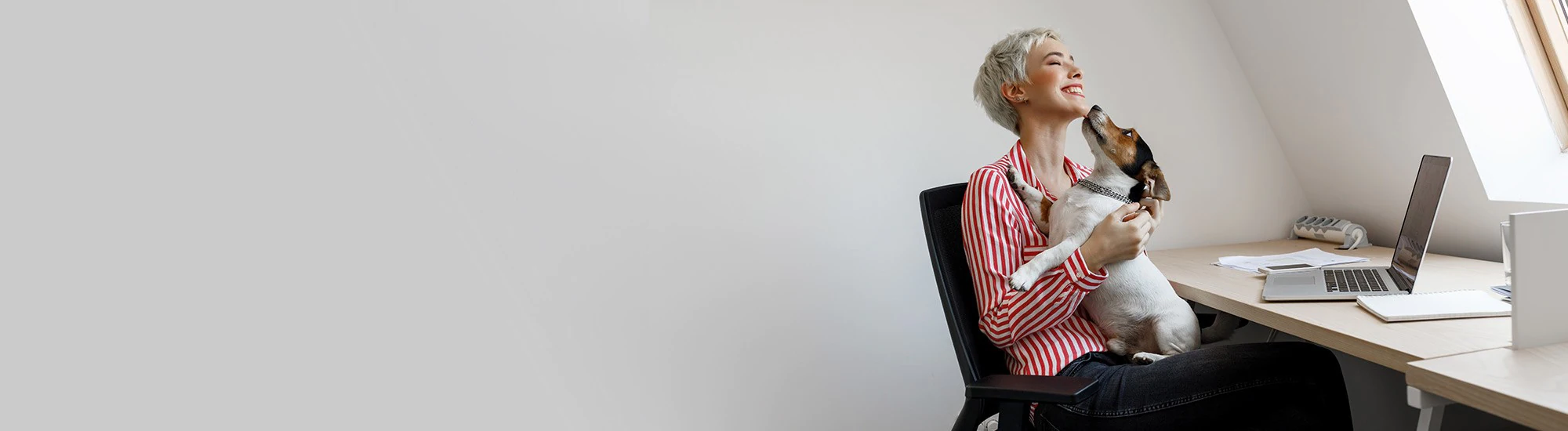 A woman's dog licks her face as she sits at her desk.