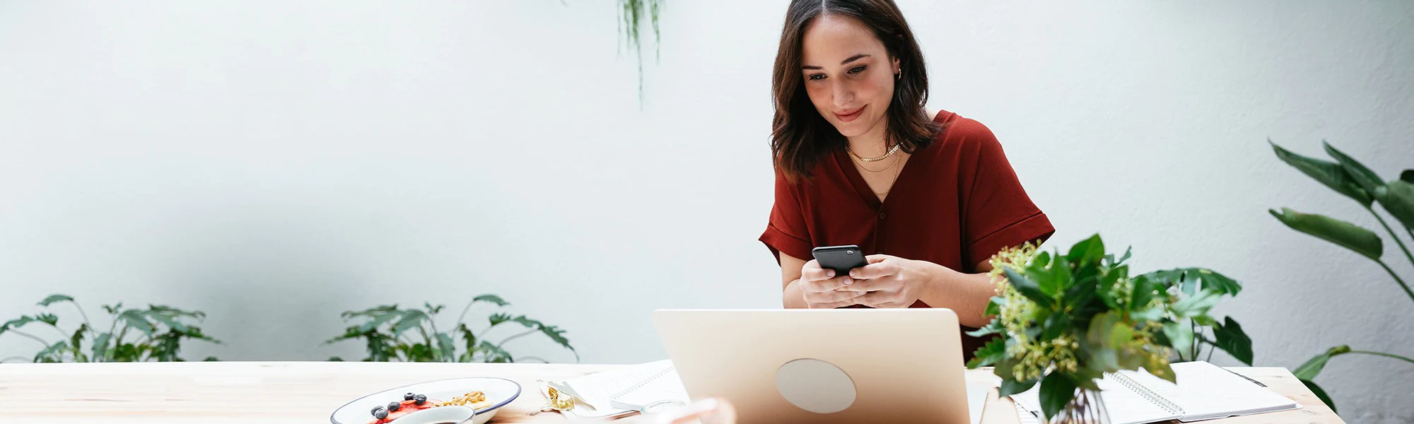 A woman glances at her laptop as she types on her phone.